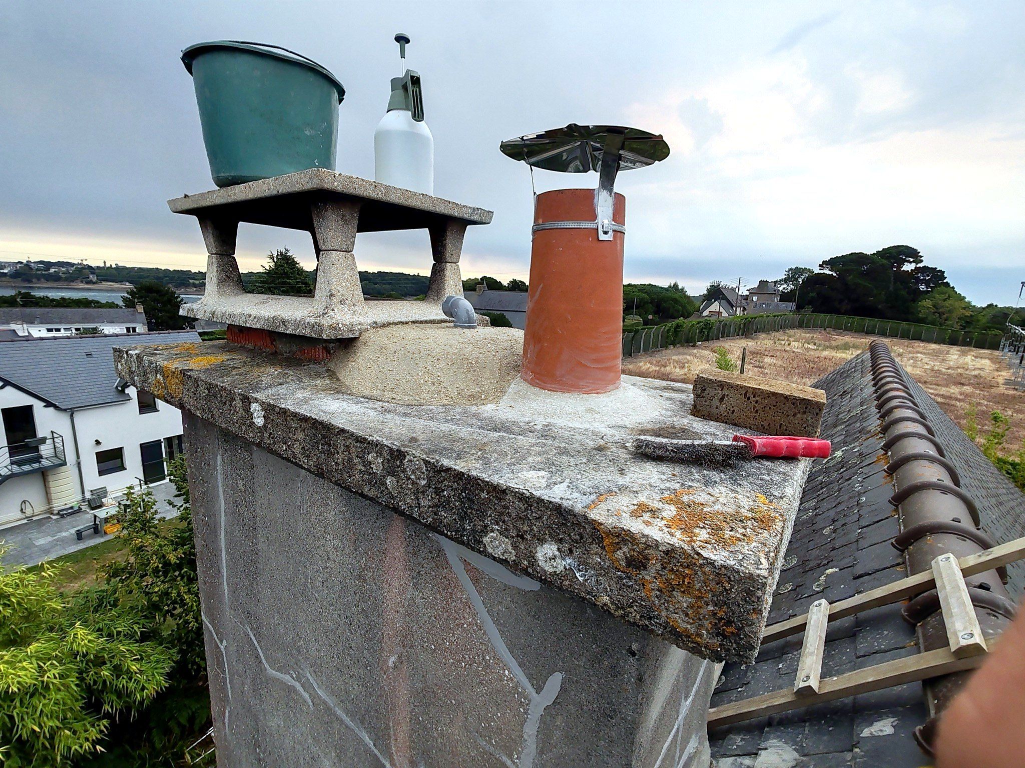 Souche de cheminée avec deux mitres en terre cuite en cours de scellement